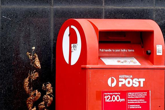 Red Australia Post mailbox with a black tiled wall background